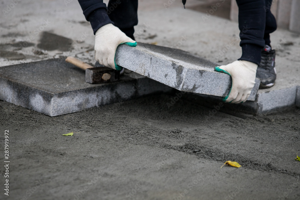 Close up of the gloved hands of a builder laying outdoor paving slabs on a prepared base. Close up of the gloved hands of a builder laying outdoor paving slabs on a prepared base.