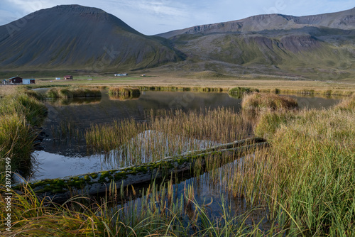 A small lake against a background of green hilly mountains. Traditional landscape of Iceland. Beautiful northern landscape.