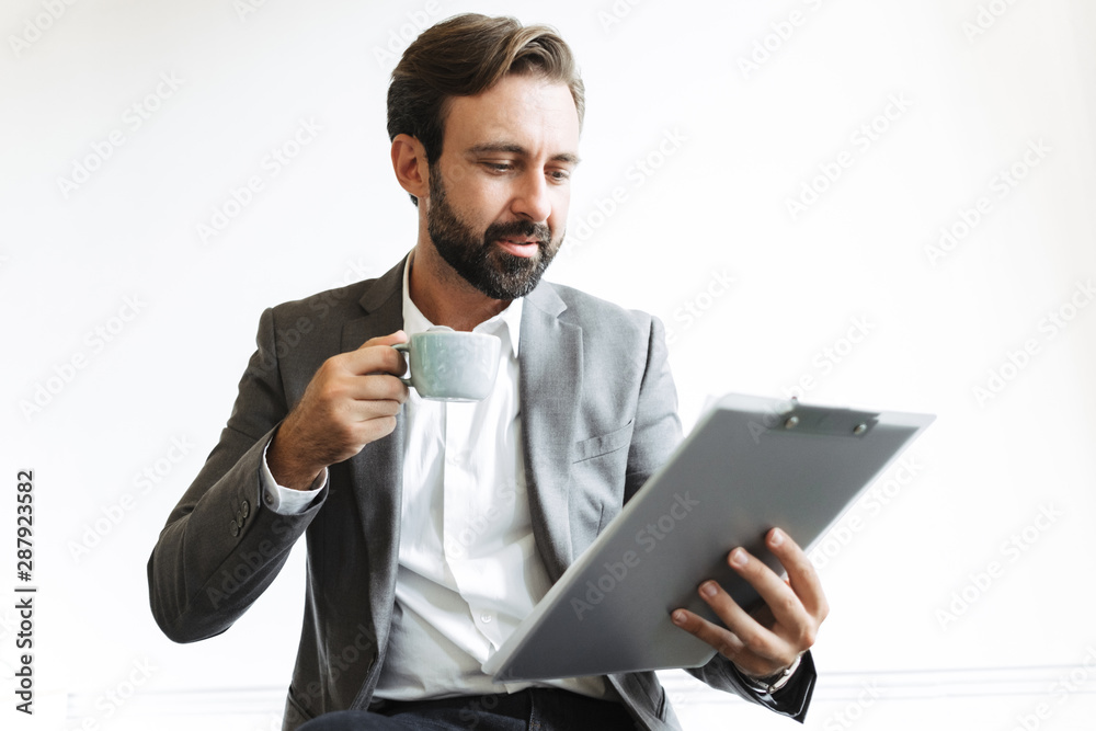 Handsome bearded business man in office drinking coffee holding clipboard. Handsome bearded business man in office drinking coffee holding clipboard.