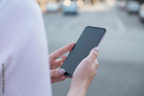 Beautiful brunette business woman in white skirt and grey suit trousers working on a mobile phone in her hands outdoors. European city on background. copy space