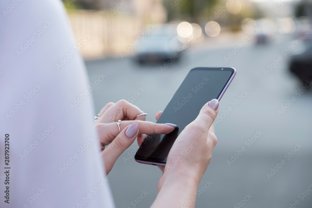 Beautiful brunette business woman in white skirt and grey suit trousers working on a mobile phone in her hands outdoors. European city on background. copy space