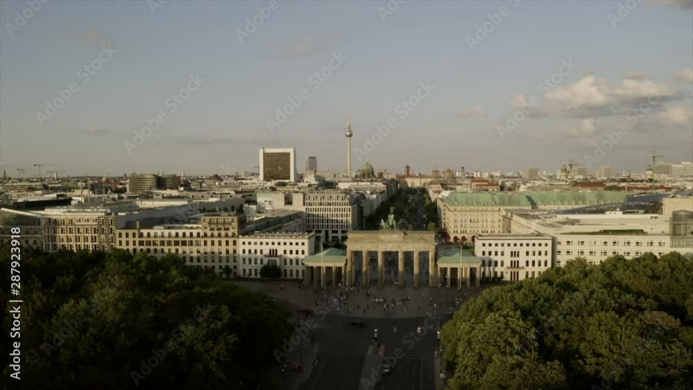 The skyline of Berlin on a summer day. The drone is flying slowly to the Brandenburg gate. People are walking around and clouds are in the blue sky. The TV tower is prominently in the background. The skyline of Berlin on a summer day. The drone is flying slowly to the Brandenburg gate. People are walking around and clouds are in the blue sky. The TV tower is prominently in the background.