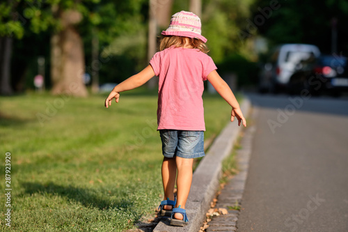 Εκτύπωση καμβά Rear view of a girl child in summer clothing balancing alone on a curb between a
