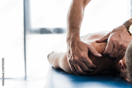 cropped view of chiropractor doing massage to shirtless patient