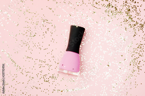 Nail polish bottle on golden glittering background. Pink fingernail varnish on nude backdrop with shiny glitters. Female cosmetics accessory. Elegant manicure enamel, pedicure lacquer top view