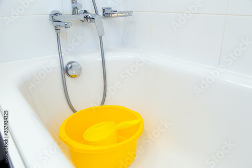 A yellow plastic basin with a dipper in the white bathroom. photo