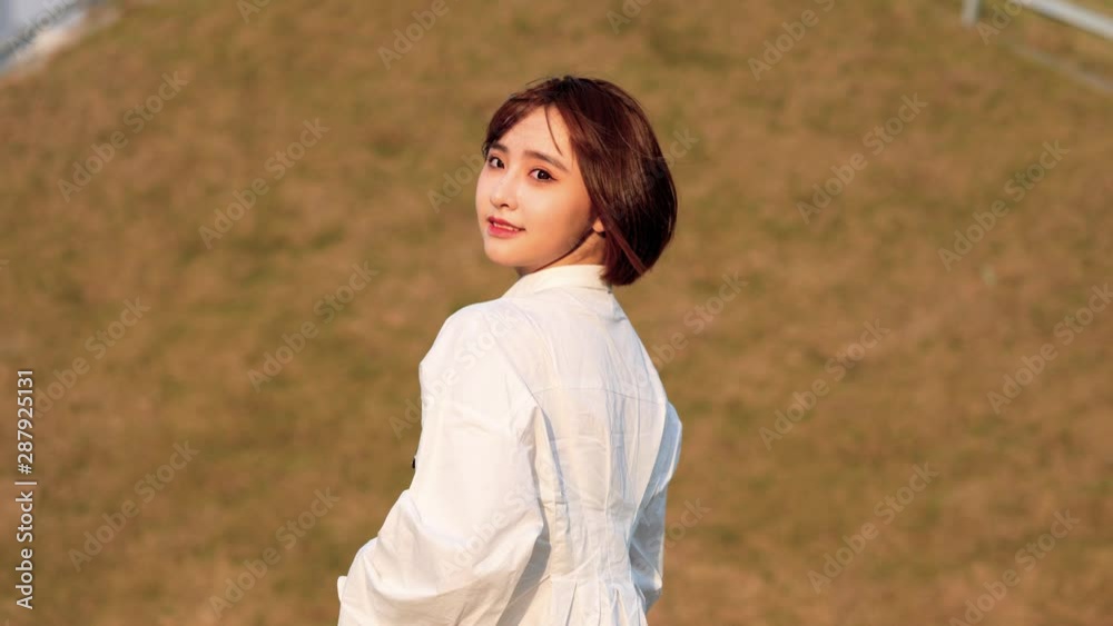 Beautiful Chinese girl in white shirt looking back and smiling at camera in windy and sunny day, sweet smile and cute blink, 4k movie, slow motion. Beautiful Chinese girl in white shirt looking back and smiling at camera in windy and sunny day, sweet smile and cute blink, 4k movie, slow motion.