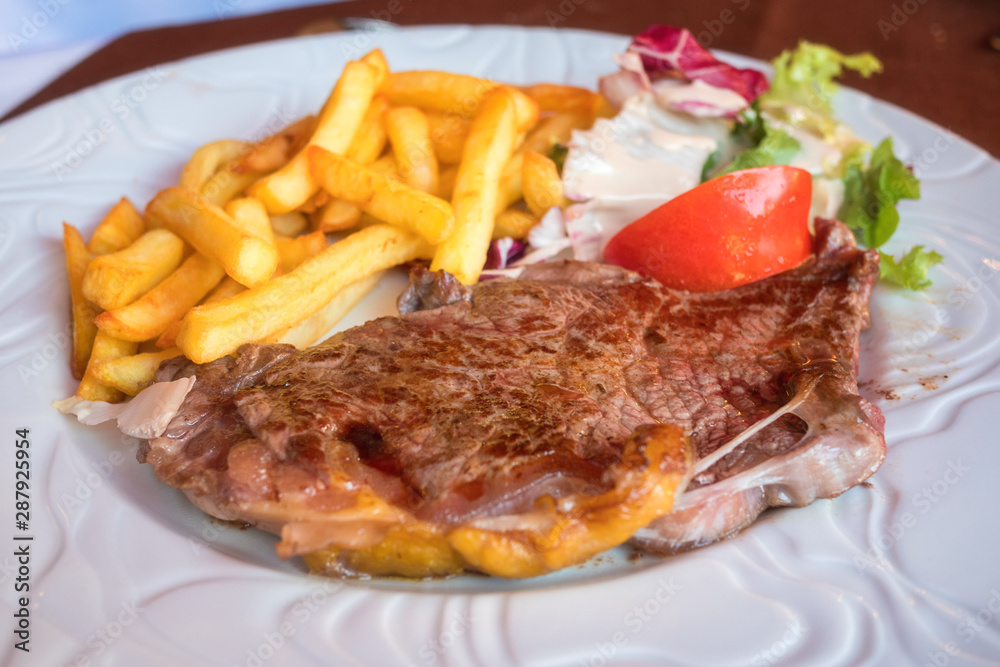 Roasted veal steak with fried potato (french fries) and salad on the white plate, served meat dish