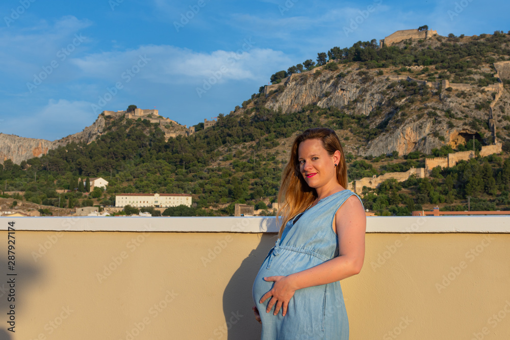 Profile view of pregnant woman with long hair in blue sky dress outdoor