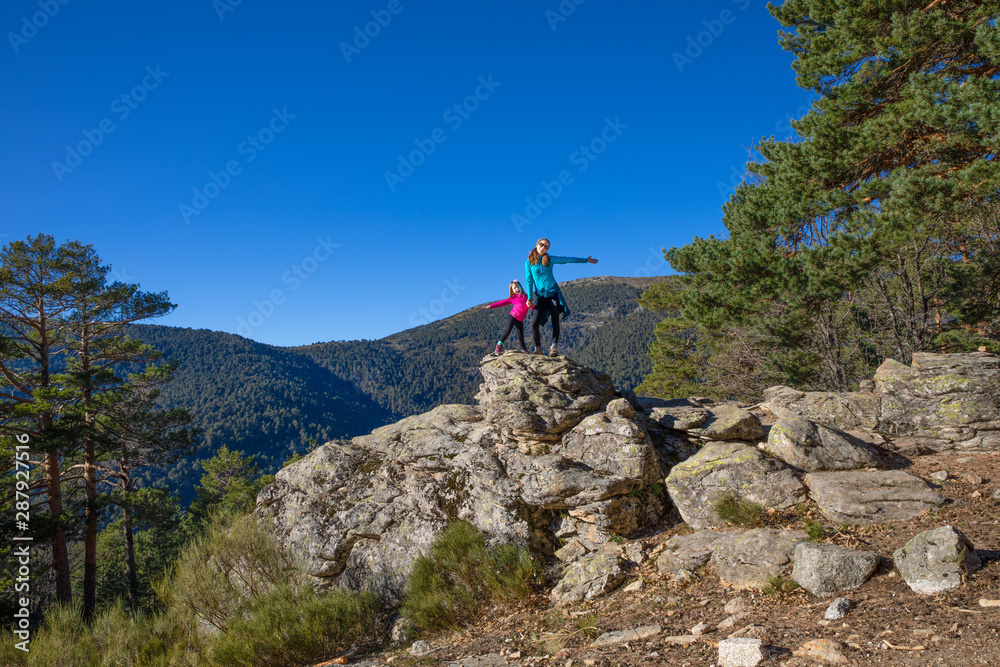 happy family (woman and five years old girl) posing on the top of rock in mountain of Fuenfria Valley, in Guadarrama Natural Park (Cercedilla, Madrid, Spain)