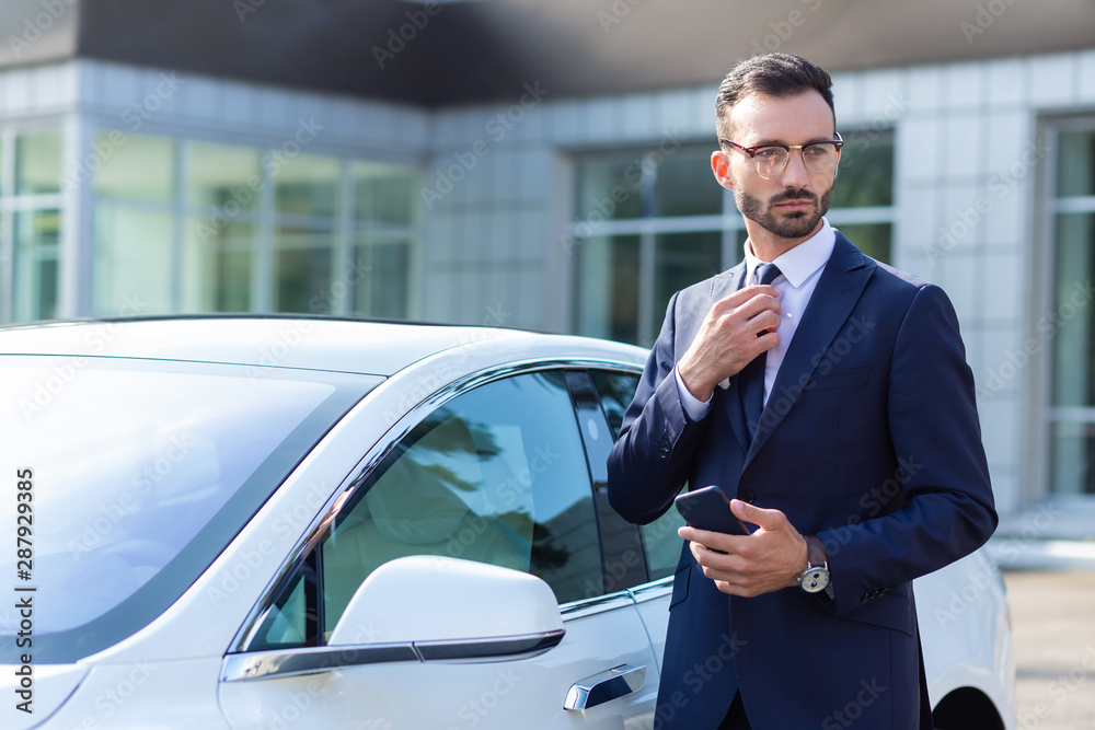 Prosperous businessman wearing glasses standing near his car Prosperous businessman wearing glasses standing near his car