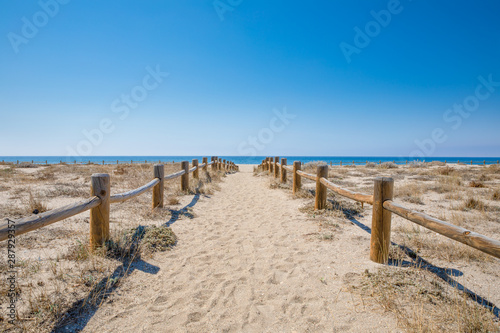 sand footpath with wooden banisters in nature to Cabo de Gata Beach, wild and beautiful famous destination, in Almeria (Andalusia, Spain, Europe). Mediterranean sea in the horizon