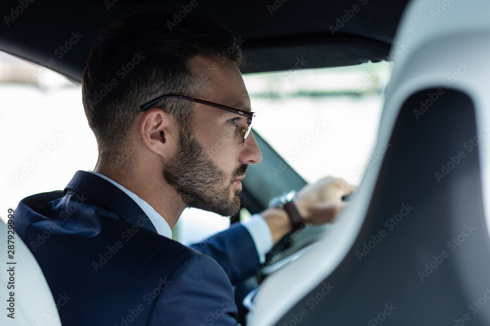 Bearded man wearing glasses looking into right side mirror