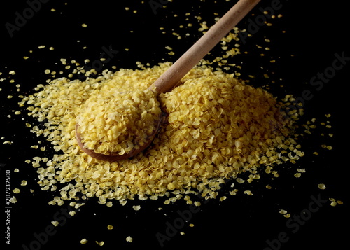 Millet flakes with wooden spoon isolated on black background