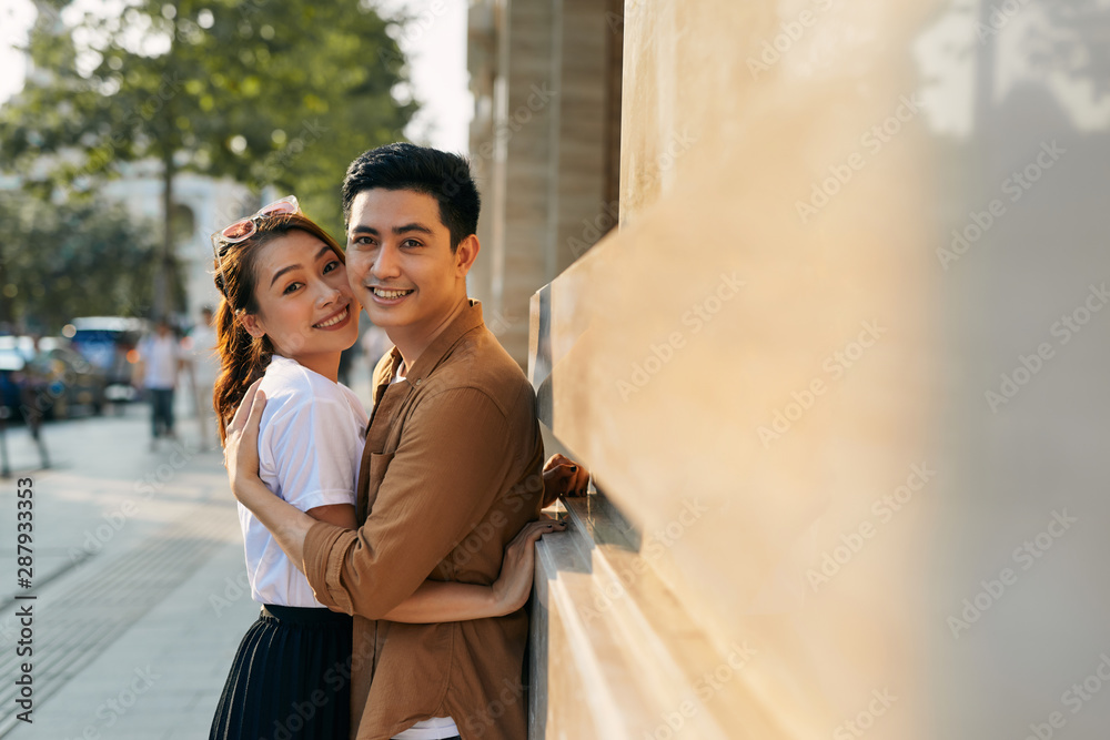 Naklejka premium Rear view of a young couple hugging in a destination city while standing in the shopping district near a luxury quality shoe store, outdoors