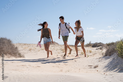 A boy and two girls are running down a sand dune