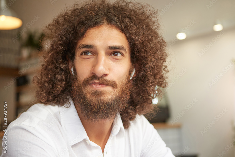 Close-up portrait of attractive young male with beard, having long curly hair and brown kind eyes, having positive attitude, wearing white shirt Close-up portrait of attractive young male with beard, having long curly hair and brown kind eyes, having positive attitude, wearing white shirt