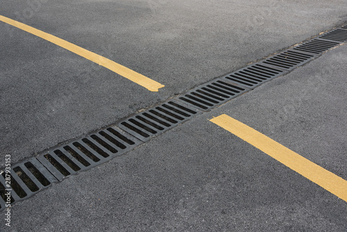 Close-up of drains and yellow paint lines on asphalt bends