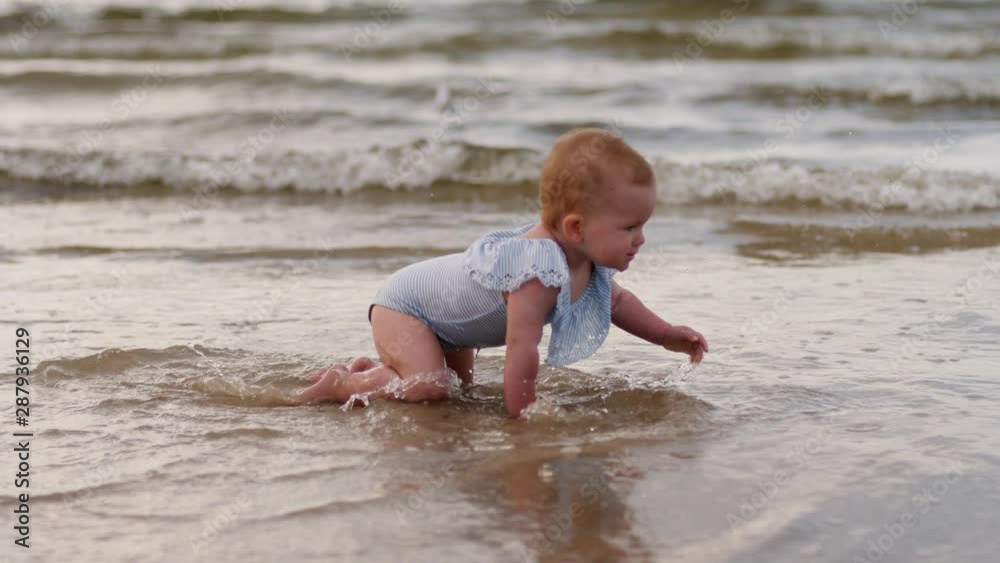 Toddler baby girl crawls in shallow waterline of Baltic sea beach shore enjoy play in water Toddler baby girl crawls in shallow waterline of Baltic sea beach shore enjoy play in water