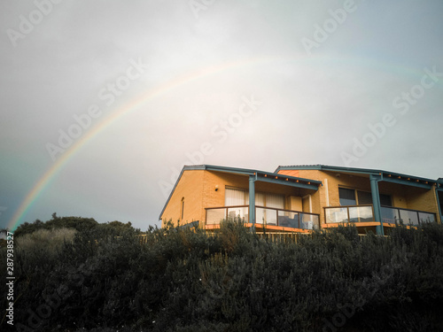 full rainbow over the house with grass in front 