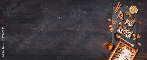 Panel kuchenny z motywem Honey products background. Honeycomb frame, bee pollen granules, honey in glass pot, almond nuts on black slate tray over dark background. Copy space. Top view. Autumn harvest concept. Banner