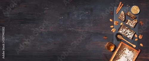 Panel kuchenny z motywem Honey products background. Honeycomb frame, bee pollen granules, honey in glass pot, almond nuts on black slate tray over dark background. Copy space. Top view. Autumn harvest concept. Banner