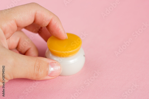 Closed jar with an orange cap with face cream on a pink background.