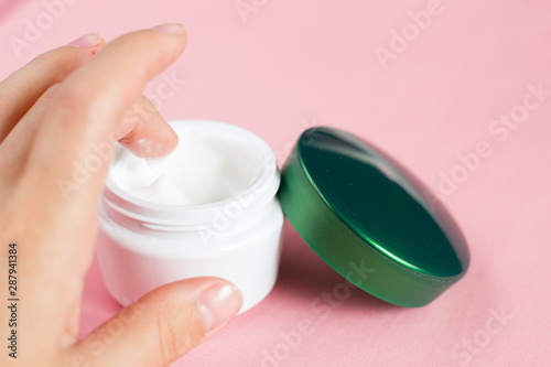 Open jar of face cream on a pink background.