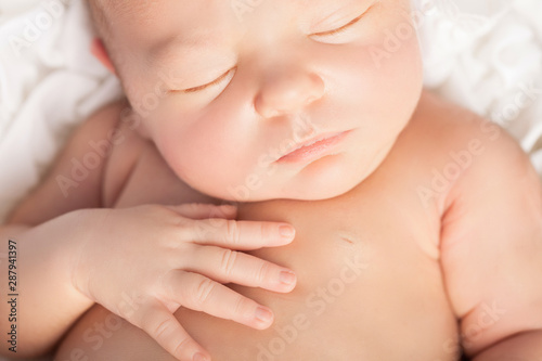 Close up of newborn baby face, asleep with hands on chest.