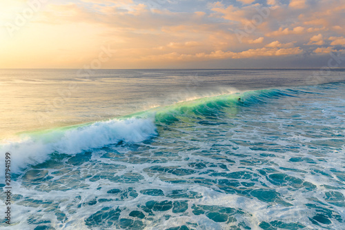 Aerial view of big waves creating sea spray at sunset in the turquoise water, Bali, Indonesia