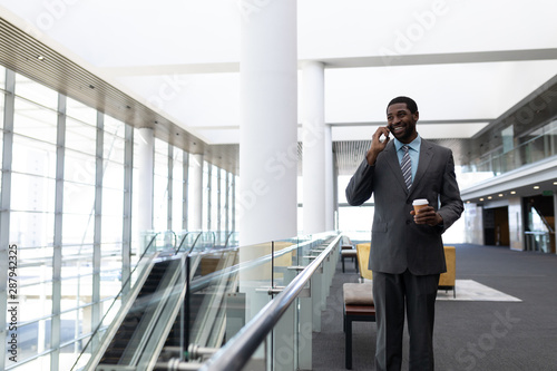African-American businessman with coffee cup talking on mobile phone in office