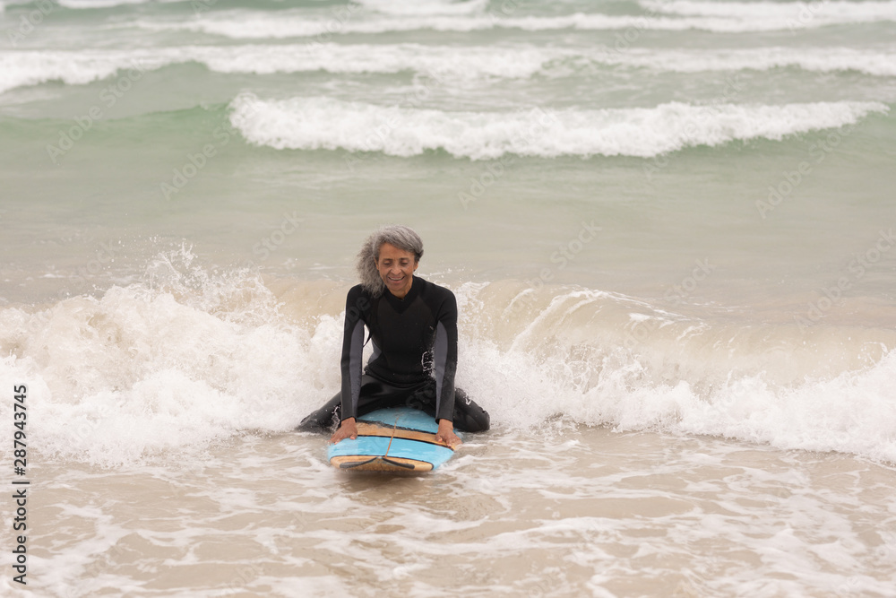 Senior female surfer sitting on surfboard in sea Senior female surfer sitting on surfboard in sea