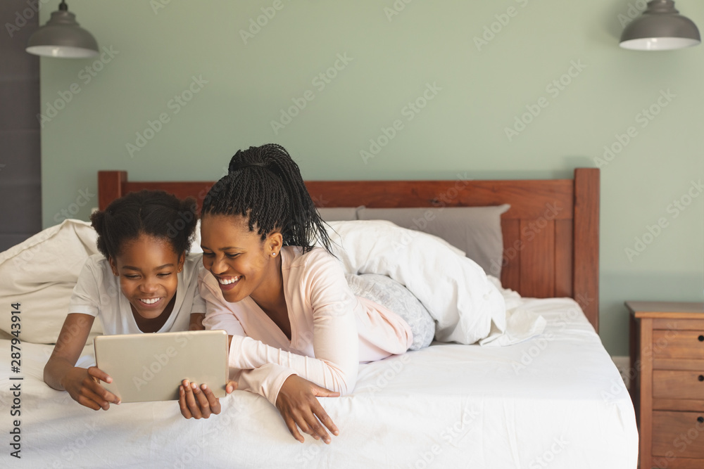 Happy African American mother and daughter lying on bed and using digital tablet Happy African American mother and daughter lying on bed and using digital tablet