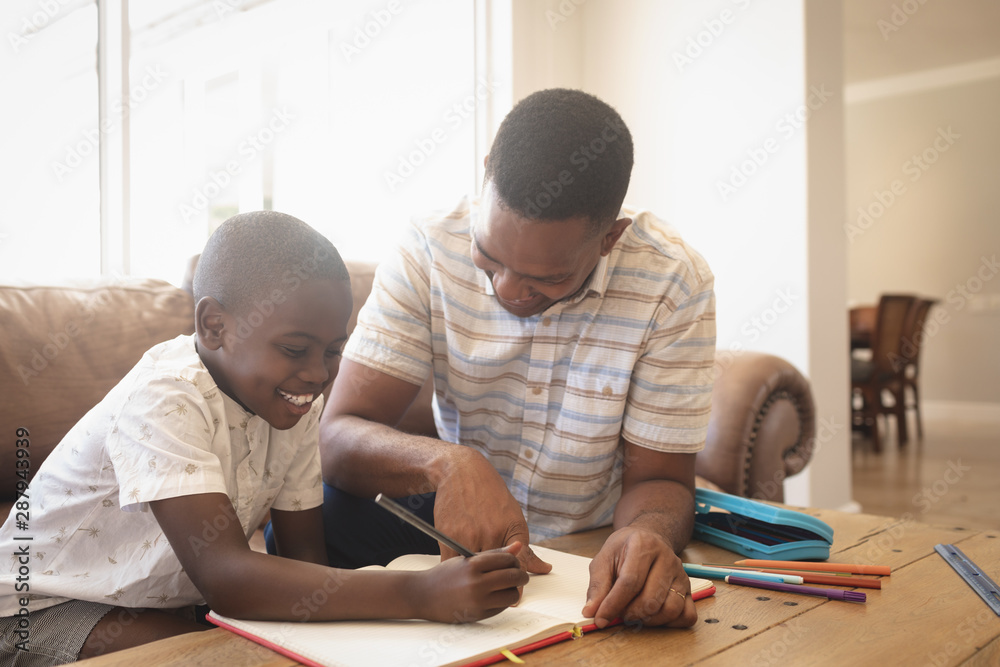 Front view of African American father helping his son with homework at table Front view of African American father helping his son with homework at table