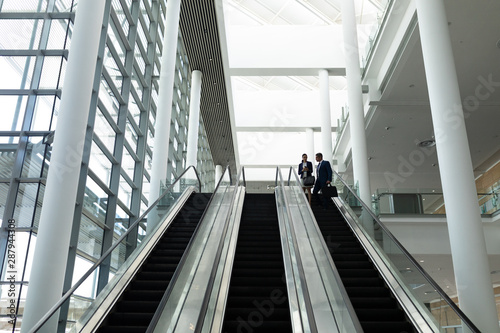 Businessman and businesswoman interacting with each other while moving down on escalator