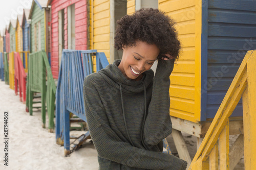 Young African American woman with hand in hair standing at beach hut