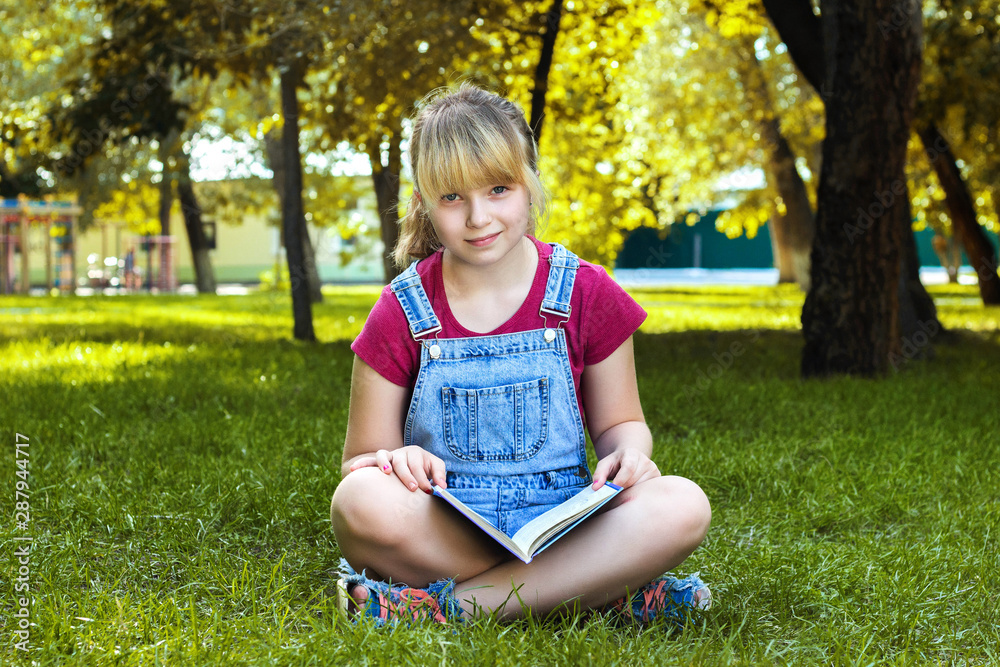 Beautiful girl reading a book sitting on the grass in the Park Beautiful girl reading a book sitting on the grass in the Park
