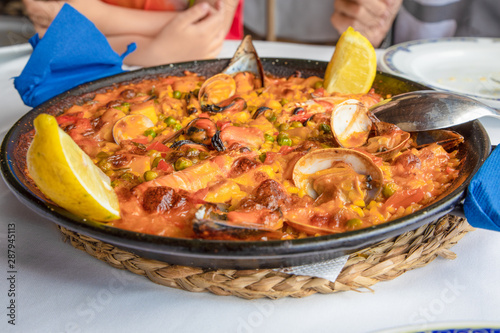 close up view of typical Spanish paella with seafood  mussel  prawn  lobster  squid  clam   rice and lemon ready to serve on white tablecloth of restaurant
