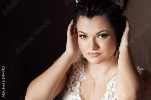  Portrait of beautiful bride with stylish make up and hair style. A elegant and beautiful bride at home. A bride in a dress corrects the crown. Pretty young girl. Wedding. Sexy bride.