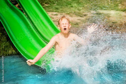 Young boy or kid has fun splashing into lake after going down water slide during summer. Vacation and childhood concept © indigolt