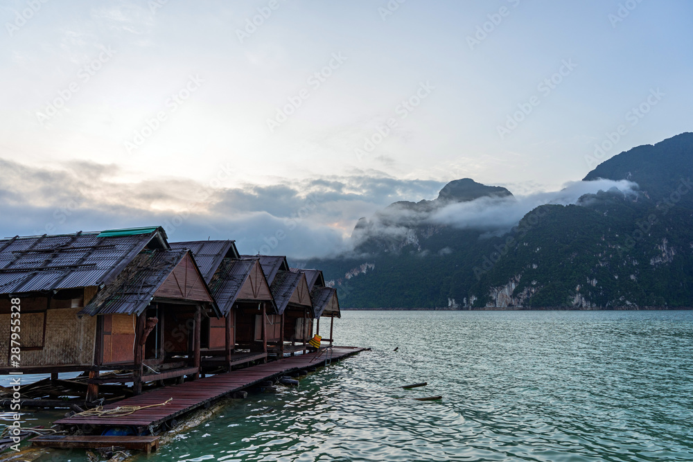 Raft houses at sunrise with clouds above water and mountain