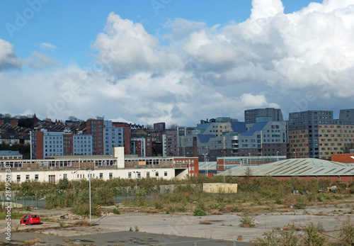 a large empty brownfield site in leeds england with weeds growing through concrete and a burned out abandoned car surrounded by city apartment buildings photo