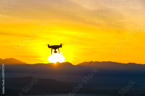 Drone quadcopter flying on mountain sunset silhouette scene © themorningglory