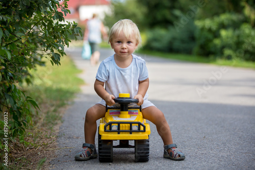 Sweet toddler boy, riding plastic toycar on the street in quiet neighborhood photo