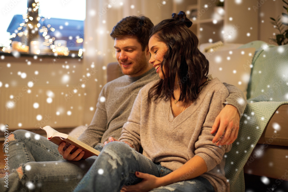 leisure, christmas and people concept - happy couple reading book at home over snow leisure, christmas and people concept - happy couple reading book at home over snow