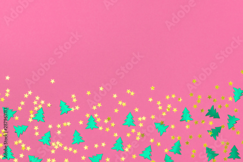 Green metallic foil christmas trees and gold stars confetti sparse on pink background. Simple holiday concept. Design template. Frame with copy space. Winter festive backdrop. Top view, flat lay.