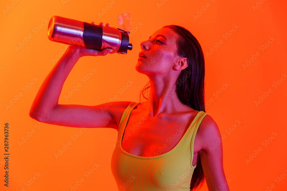 Photo of pretty brunette woman wearing formfitting sportswear drinking water from metal bottle while doing workout Photo of pretty brunette woman wearing formfitting sportswear drinking water from metal bottle while doing workout