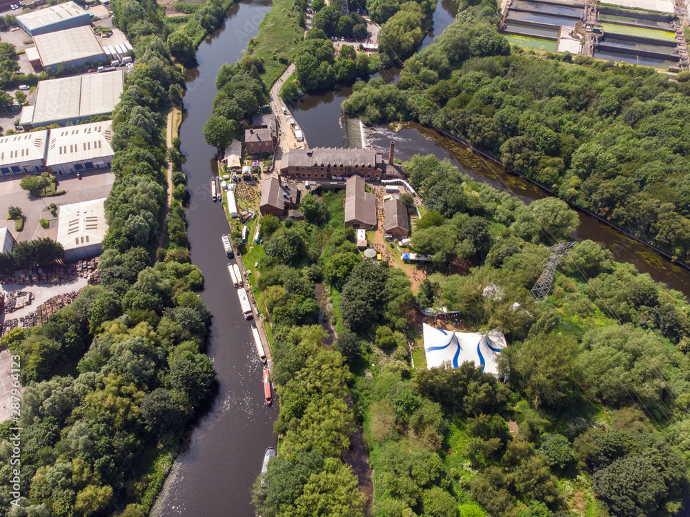 Aerial footage of The Made in Leeds Festival located at the Thwaite Mills along the side of the Leeds Canal showing the water and waterfall on a sunny day