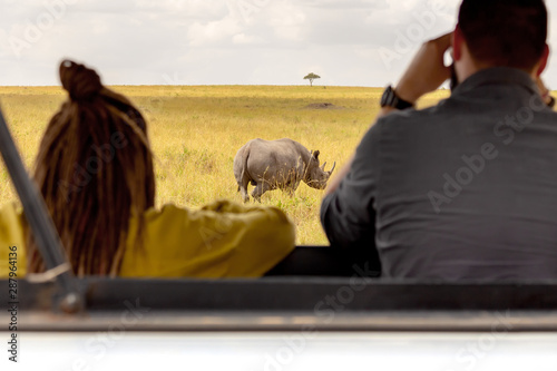Safari concept. Tourists in Safari car looking at rhinoceros in african savannah. Masai Mara national park, Kenya. photo