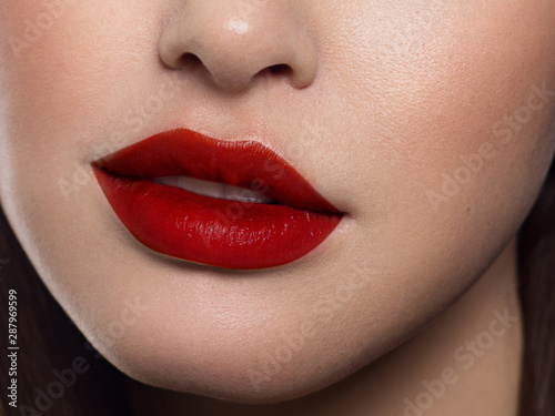Beauty closeup of women full red lips with shiny skin and long hair. Facial skin care in a spa salon or cosmetology and a fashionable red lip gloss. Evening makeup